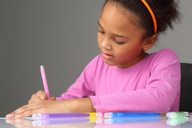 A menina desenha com lápis de cor no papel