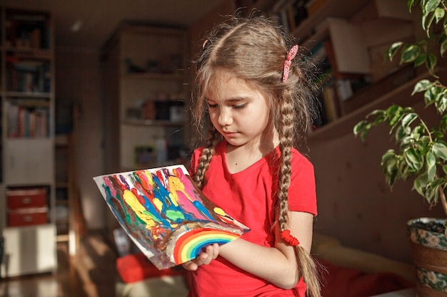 A menina desenha o arco-íris com lápis de cera derretido usando o secador de cabelo e estrelas de cera para derreter a ideia de arte