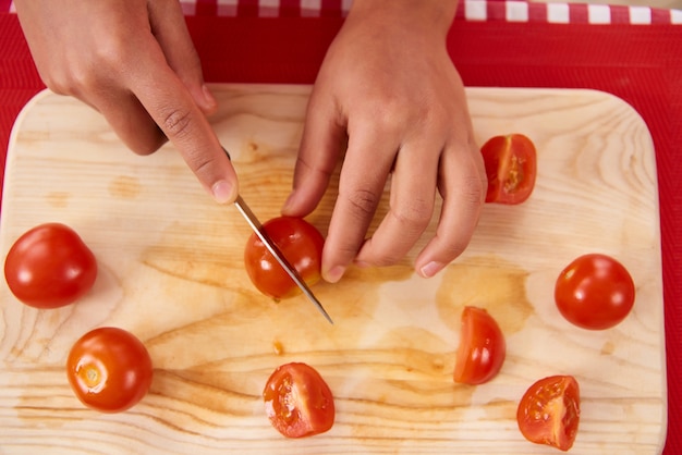 A menina do americano africano corta tomates na placa da cozinha.