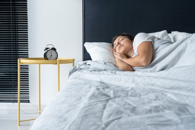 A menina dorme ao lado do despertador. Hora de acordar. No relógio de despertar 7 horas da manhã. Sono profundo.