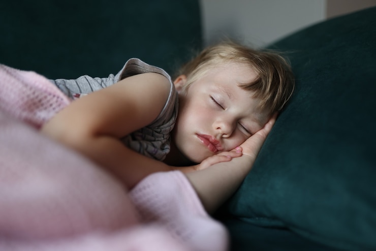 Foto a menina dorme na cama com os braços cruzados sob a cabeça.