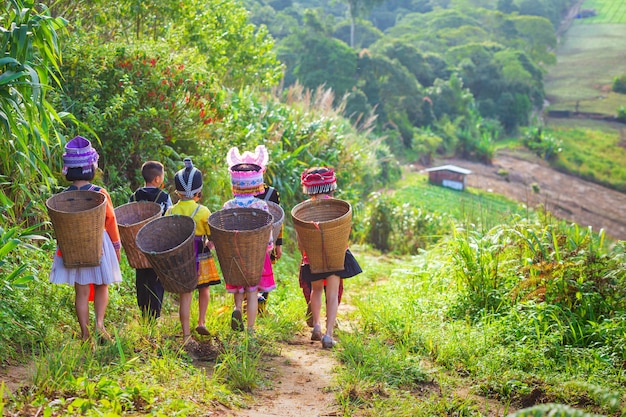 A menina e menino vestindo um vestido Hmong transportar cesta de bambu nas costas dela no caminho para thei