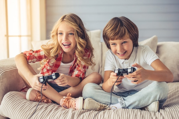 A menina e o menino bonitos estão jogando o console do jogo.