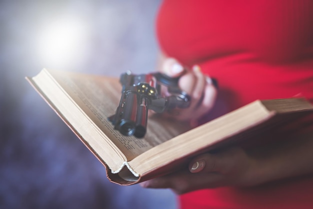 A menina em um vestido vermelho puxa a arma no livro isolado no cinza