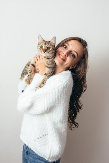 A menina em uma camisola branca abraça um gato cinzento em um branco