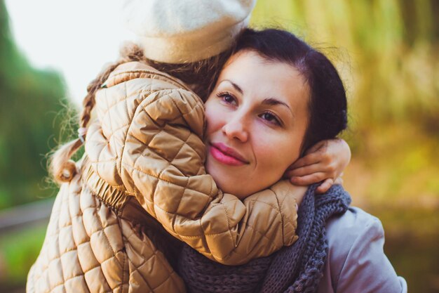 A menina em uma jaqueta cor de mostarda abraça sua mãe