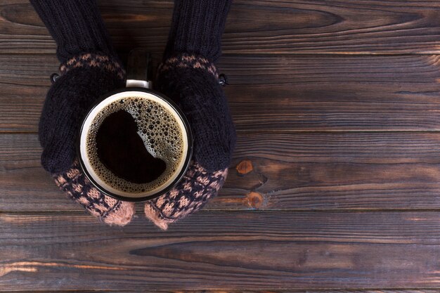 A menina em uma roupa e em luvas mornas está guardando a caneca branca nas mãos.