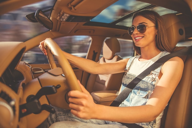 A menina em vidros de sol está sorrindo ao conduzir o carro.