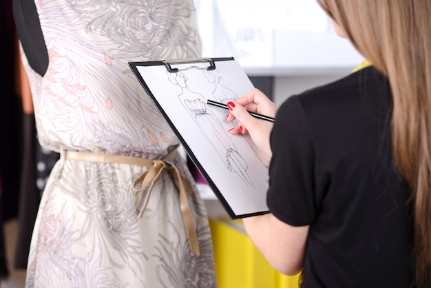 A menina esboça um vestido no papel no estúdio.