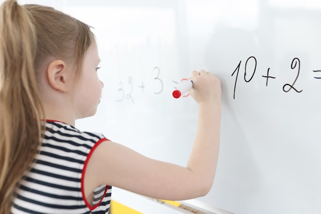 A menina escreve exemplos matemáticos no quadro branco