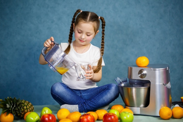 A menina espremeu suco fresco de frutas de maçãs e laranja. Vitaminas e alimentação saudável para crianças.