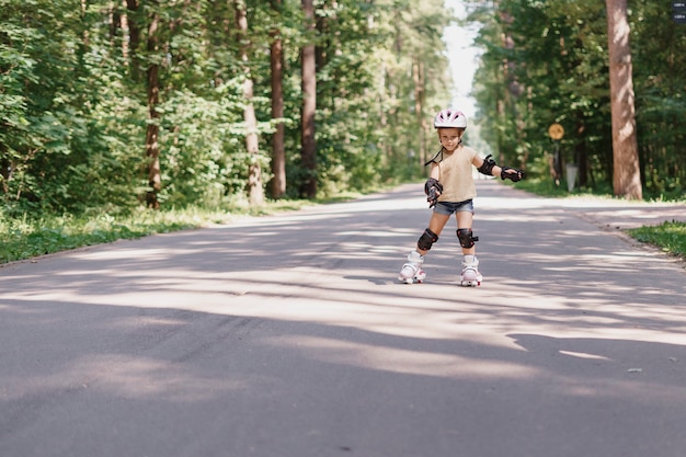 A menina está andando de patins no parque. bebê em roupas esportivas de proteção