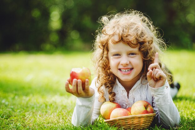 A menina está comendo a maçã e está sorrindo mostrando os dentes brancos.