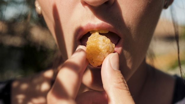 Foto a menina está comendo baga. mulher jovem coloca framboesas na boca em um dia ensolarado. vista de perto