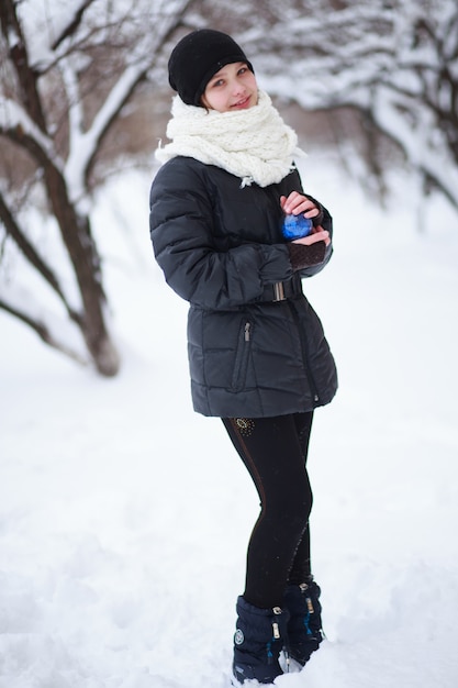 A menina está de pé contra o fundo de galhos cobertos de neve e tem nas mãos um brinquedo de árvore de pele azul