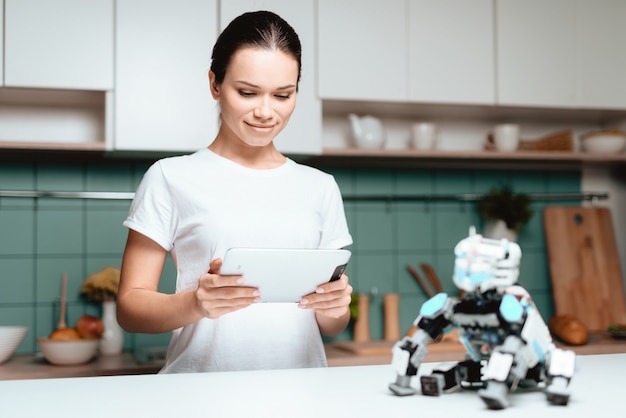 A menina está de pé na cozinha e segurando um tablet.