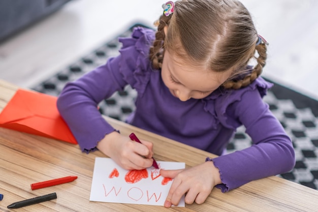 A menina está desenhando um cartão de felicitações para sua mãe com forma de saúde vermelha feliz dia das mães