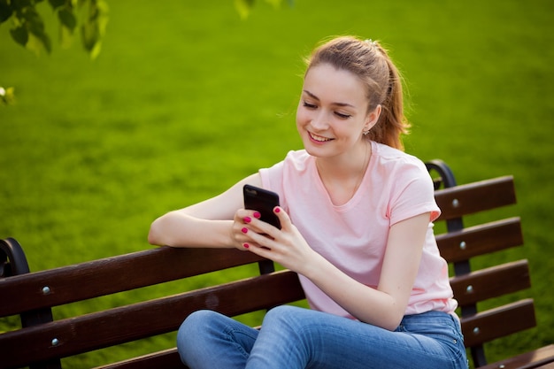 A menina está enviando mensagens de texto no telefone enquanto está sentada no parque