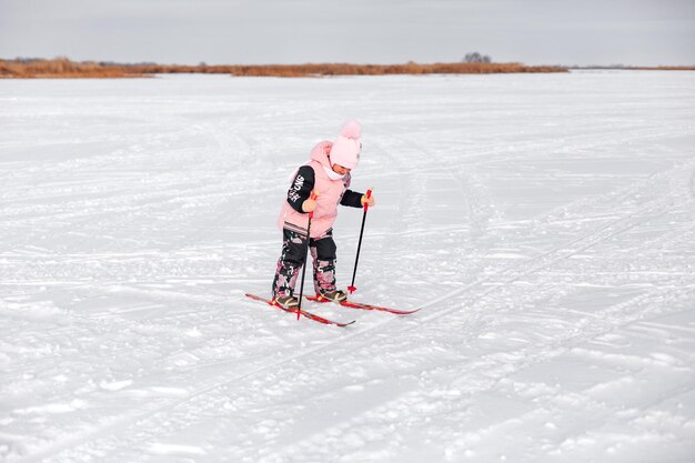 A menina está esquiando, uma criança em um terno quente rosa aprende a esquiar na neve em um dia gelado de inverno.