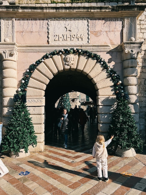 A menina está na frente de um arco antigo e aponta para uma árvore de natal decorada