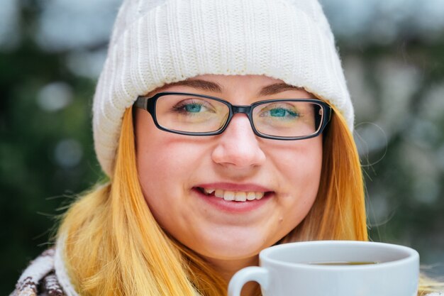 A menina está no inverno pela neve e segurando uma caneca de chá quente. luz natural, fundo claro