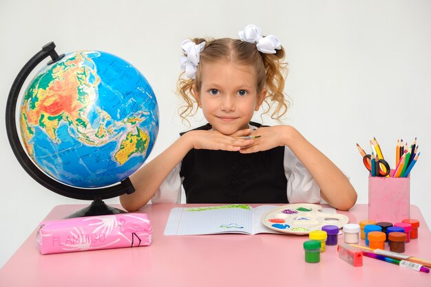 A menina está pintando com guache enquanto está sentada à mesa isolada sobre o branco