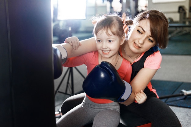 Foto a menina está praticando boxe, a menina ensina a mãe a boxe, a mãe e a filha engraçadas na academia, a mãe e a filha felizes na academia