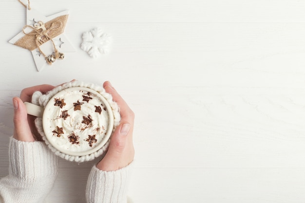 A menina está segurando um copo de bebida quente de inverno, com chantilly e pó em forma de estrelas