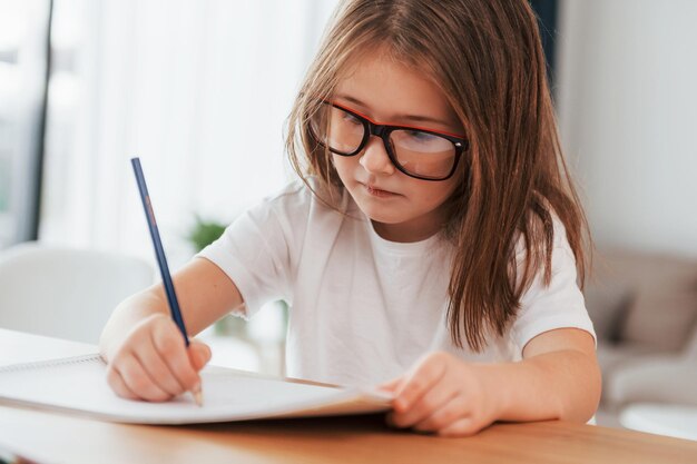 A menina está sentada à mesa e aprendendo a desenhar