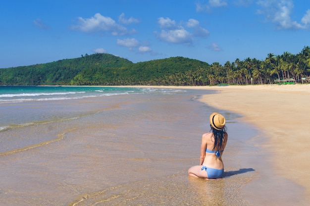 A menina está sentada em uma praia deserta.