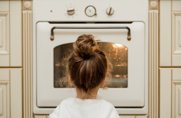 Foto a menina está sentada perto do forno e esperando a comida na cozinha.