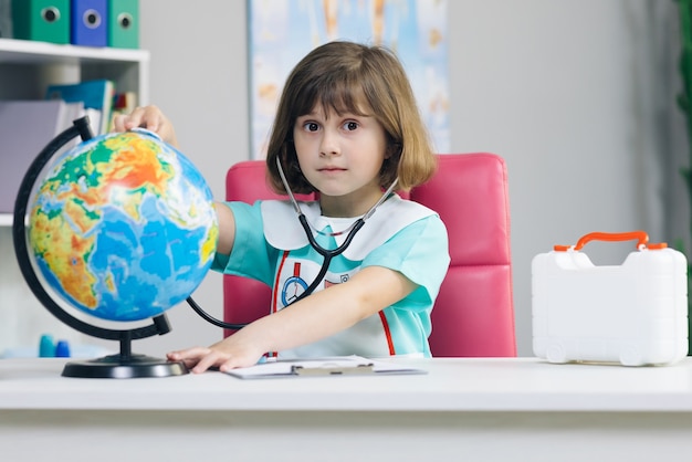 A menina está vestida com roupas de médico com um estetoscópio nas mãos, examina e joga um jogo de cura do planeta Terra.