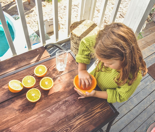 A menina faz suco de laranja espremido na hora em um espremedor manual