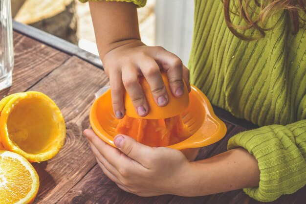 A menina faz suco de laranja espremido na hora em um espremedor manual