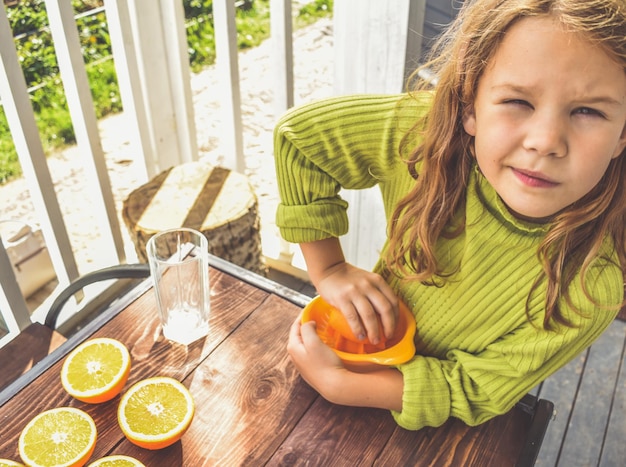 A menina faz suco de laranja espremido na hora em um espremedor manual