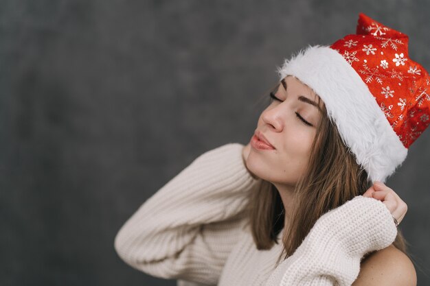 A menina faz um desejo para o ano novo. Mulher de chapéu de Papai Noel vermelho. Menina sonhando com um chapéu de Papai Noel.