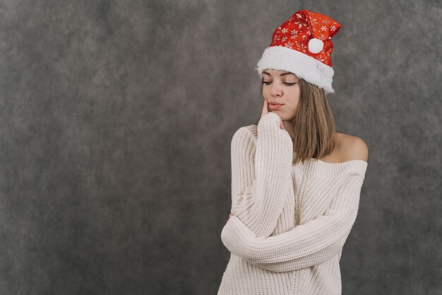 A menina faz um desejo para o ano novo. Mulher de chapéu de Papai Noel vermelho. Menina sonhando com um chapéu de Papai Noel.