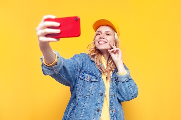 A menina faz um selfie em um smartphone em um fundo amarelo que um blogueiro transmite em um telefone