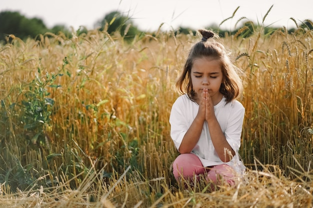 A menina fechou os olhos, orando em um campo de trigo. Mãos postas em oração. Conceito de religião