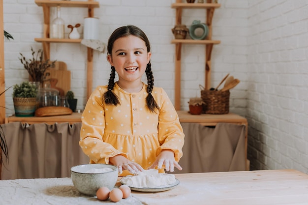 A menina feliz cozinha uma torta na cozinha em um vestido de algodão