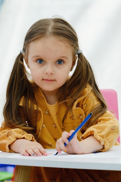 A menina feliz do miúdo europeu desenha a pintura com lápis colorido