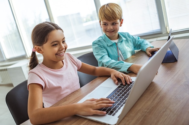 A menina feliz e um menino com gadgets sentados na mesa