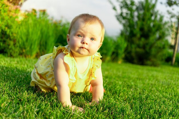 A menina feliz rasteja e anda no gramado verde no verão no parque