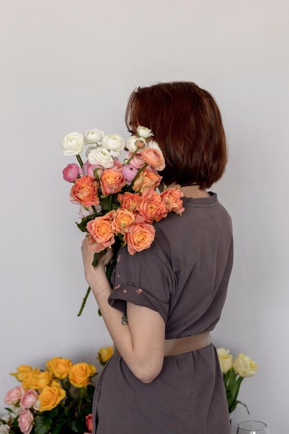 A menina fica de costas com um ramo de flores Rosas e ranúnculo