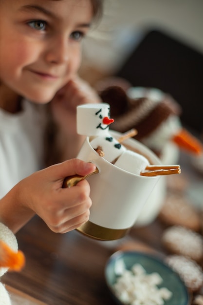 A menina fofa brinca com bonecos de neve tricotados, come pão de mel e bebe chocolate com marshmallows