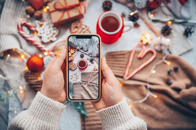 A menina fotografa a decoração de ano novo um telefone com uma foto nas mãos