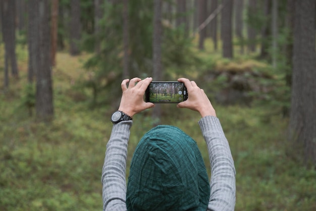 A menina fotografa a floresta com um telefone celular Vista traseira