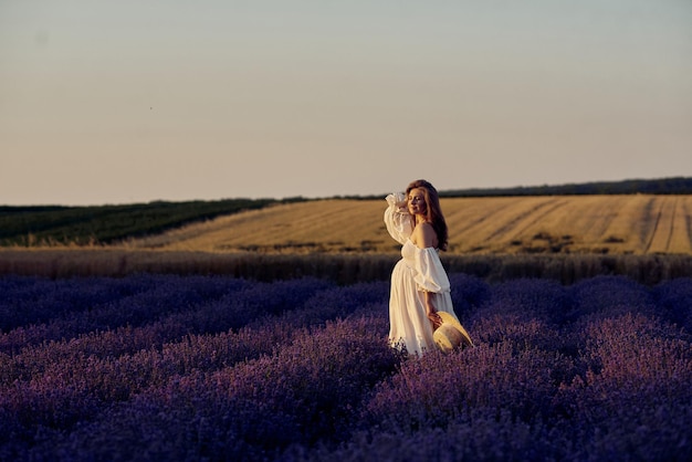 A menina grávida com um chapéu no campo de lavanda em um pôr do sol