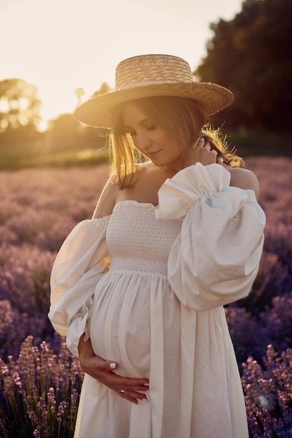 A menina grávida com um chapéu no campo de lavanda em um pôr do sol