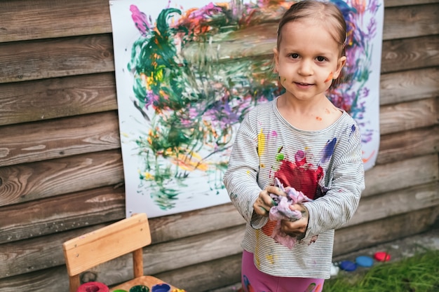 A menina limpa o pincel com um pano depois de pintar no quintal. Conceito de arte